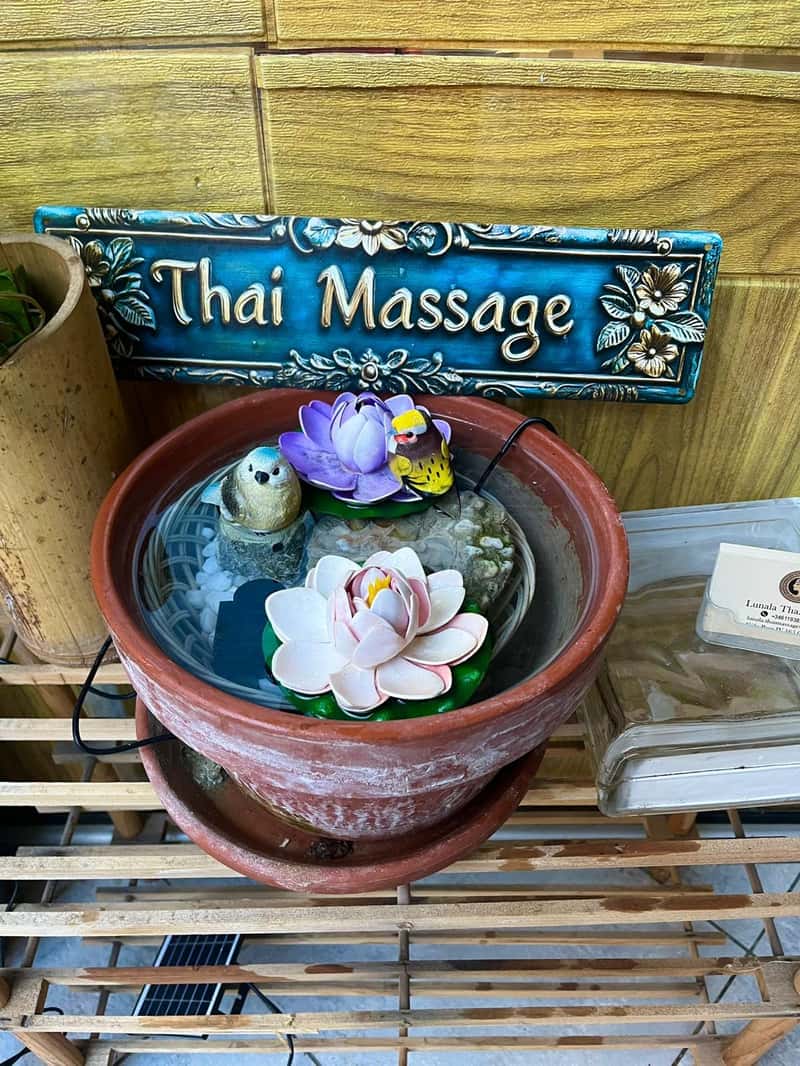 Small clay fountain with lotus flowers and bird figures, under a "Thai Massage" sign
